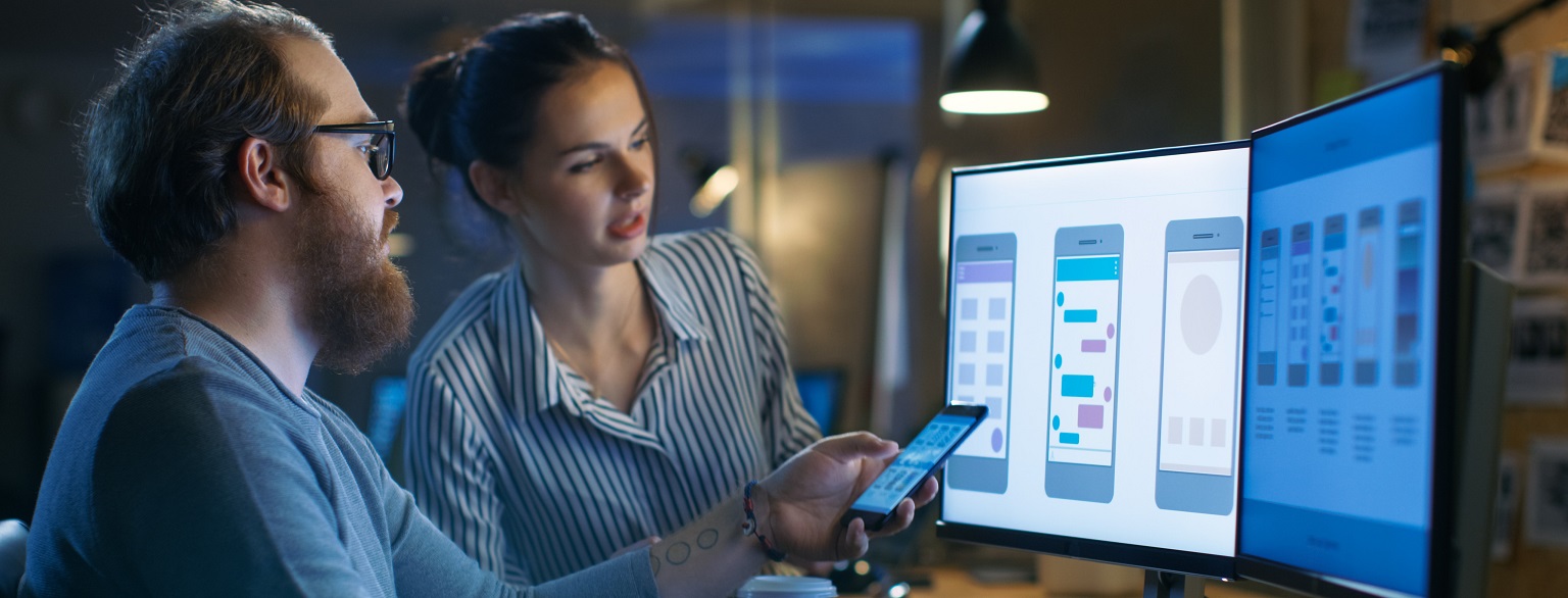 Een man en een vrouw zitten achter computerschermen
